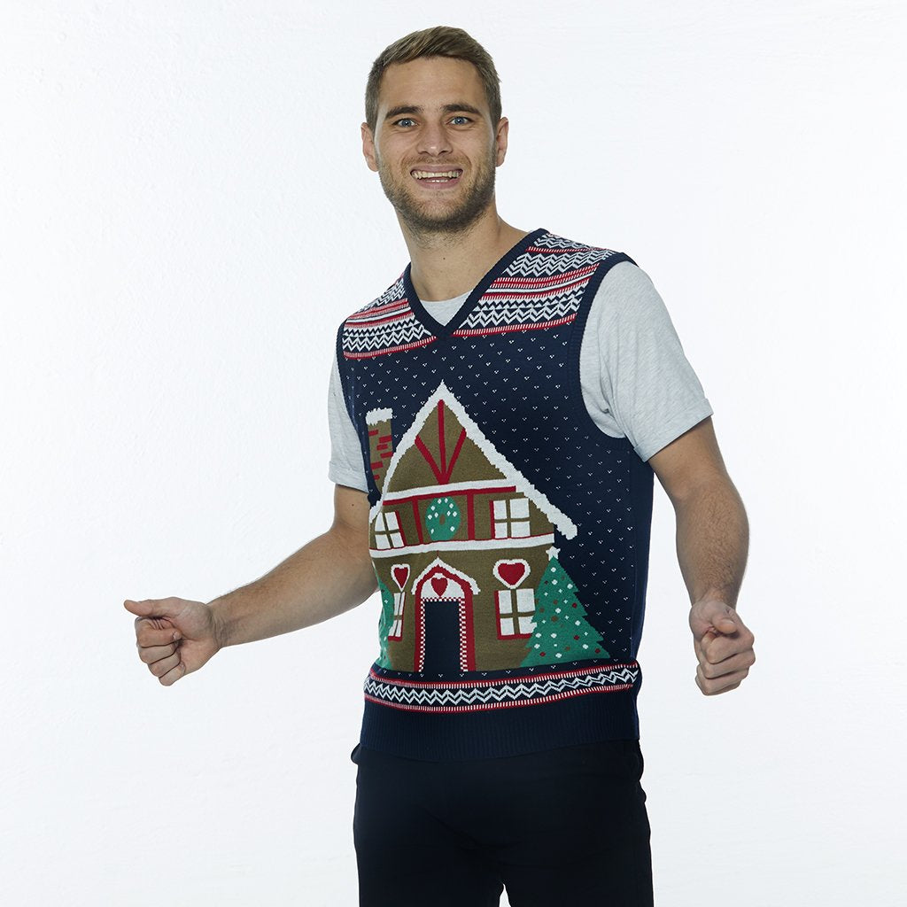 Un homme posant avec un gilet de Noël orné d'une maison en forme de gâteau.